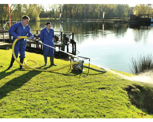 Zwei Arbeiter bedienen eine Wasserpumpe am Ufer eines Sees zur Wasserförderung.