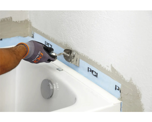Ein Handwerker verwendet einen Spachtel zum Auftragen von Dichtmasse im Badezimmer entlang einer Badewanne mit PCI Dichtband.