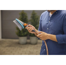 Eine Person hält eine Waschbürste mit Wasseranschluss in der Hand.