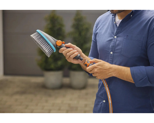 Eine Person hält eine Waschbürste mit Wasseranschluss in der Hand.