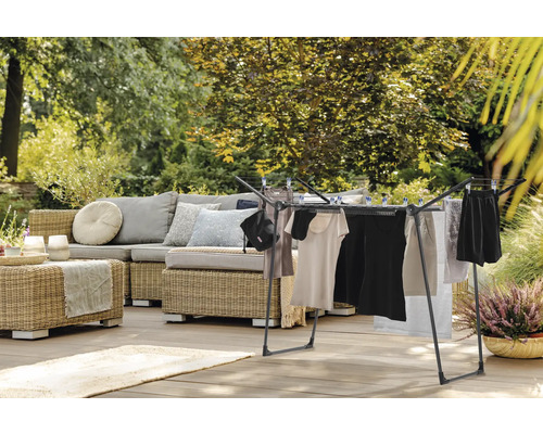 Wäscheständer auf einer Terrasse mit Sitzgruppe und Garten im Hintergrund.