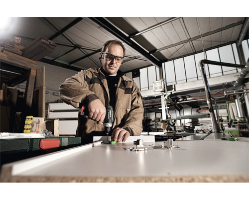 Handwerker mit Akkuschrauber bei der Montage von Möbelbeschlägen auf einer Holzplatte