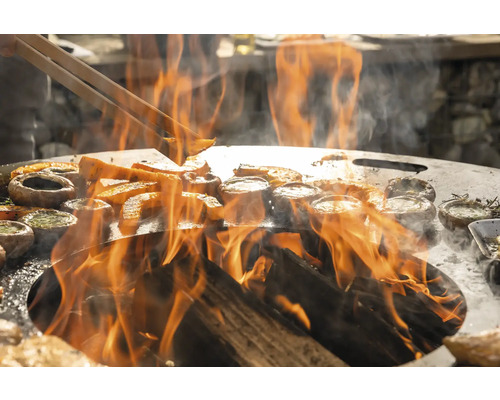 Gemüse und Pilze werden auf einer Grillplatte über offenem Feuer zubereitet.