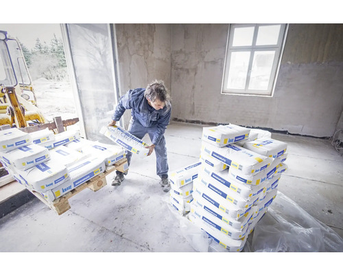 Mann lädt Säcke mit Innenputz in einem Raum ab. Palettenweise Innenputz wird angeliefert.