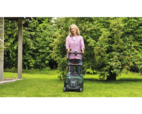 Frau bedient einen Rasenmäher im Garten.