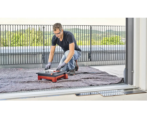 Ein Mann schneidet mit einer Fliesenschneidmaschine Fliesen auf einem Balkon.