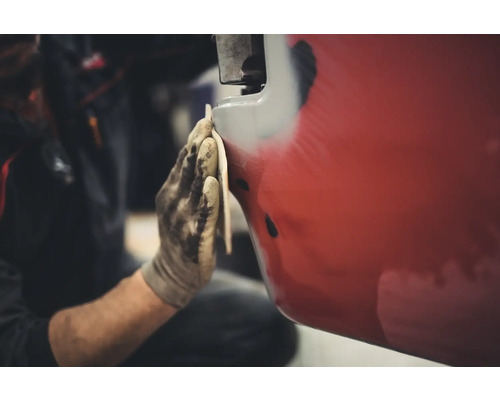 Eine Person schleift ein rotes Fahrzeug mit Schleifpapier.