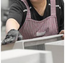 Eine Person mit Handschuhen und einer karierten Schürze hantiert mit weißen Produkten.