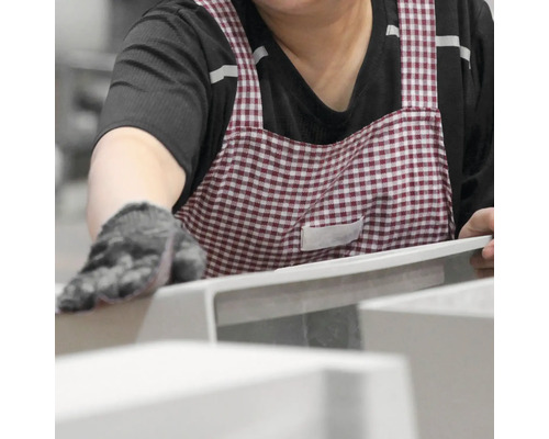 Eine Person mit Handschuhen und einer karierten Schürze bearbeitet ein Produkt.