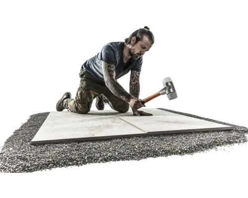 Mann verlegt Steinplatten mit Gummihammer auf Kiesbett