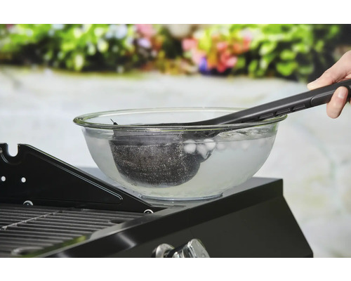 Reinigung eines Grillkorbs in einer Schüssel mit Eiswasser mit einer Grillzange.