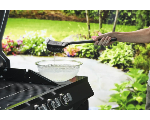 Person reinigt Grillrost mit Grillbürste über einer Schüssel Wasser.