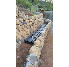 Drainagesystem Installation entlang einer Steinmauer im Garten.