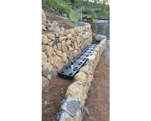 Drainagesystem Installation entlang einer Steinmauer im Garten.