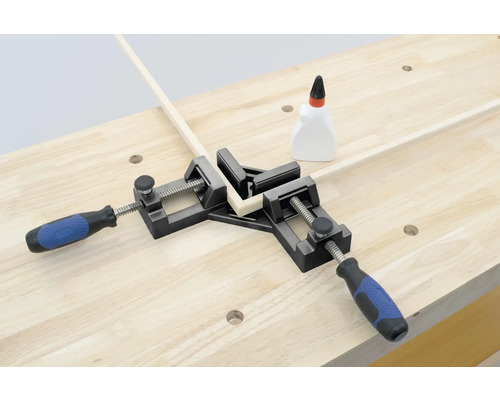 Eine Eckzwinge hält zwei Holzstücke im 90-Grad-Winkel auf einer Werkbank.