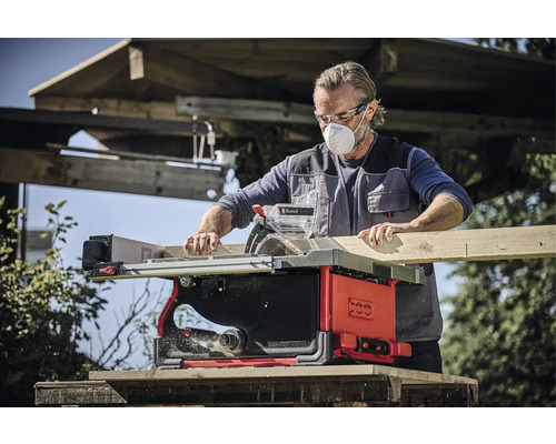 Mann mit Schutzmaske und Schutzbrille beim Sägen eines Holzbretts mit einer Einhell Tischkreissäge