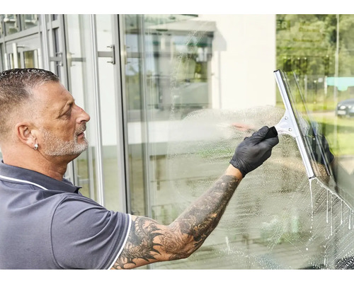 Mann reinigt Fenster mit einem Fensterabzieher