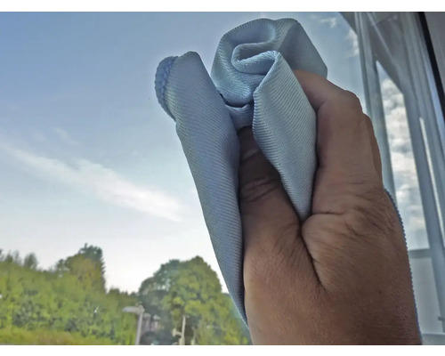 Eine Hand wischt mit einem Reinigungstuch über eine Fensterscheibe