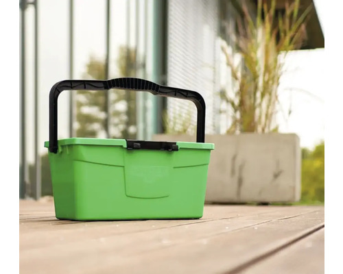 Grüner Tragekorb mit schwarzem Griff auf Holzterrasse