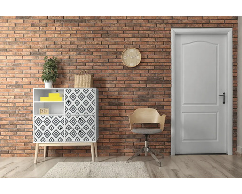 Wohnraum mit Kommode, Stuhl und Tür vor einer Backsteinwand.