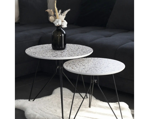 Zwei runde Beistelltische mit Terrazzo-Muster und schwarzen Metallbeinen stehen auf einem Teppich.