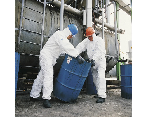 Zwei Arbeiter in Schutzanzügen bewegen ein Fass in einer Industrieanlage.