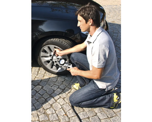 Mann pumpt Autoreifen mit einem Reifendruckmesser auf.