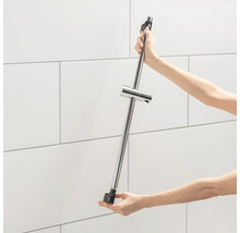 Eine Person hält eine Duschstange mit einem Brausehalter vor einer gefliesten Wand.