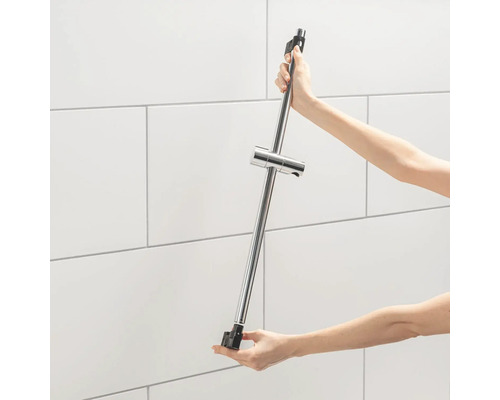 Person hält eine Duschstange aus Metall vor einer gefliessten Wand.
