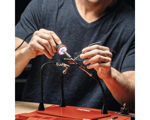 Person lötet mit einer Lötstation auf einer Arbeitsfläche.