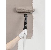Maler mit Farbroller und Teleskopstiel beim Streichen einer Wand