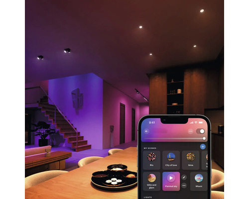 Ansicht eines Wohnzimmers mit Deckenleuchten, Treppe und einer Smartphone-App zur Lichtsteuerung.