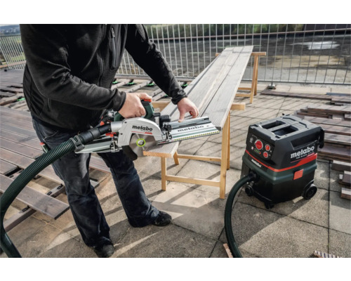 Mann schneidet Holzdiele mit einer Handkreissäge von Metabo. Ein Metabo Staubsauger steht daneben.
