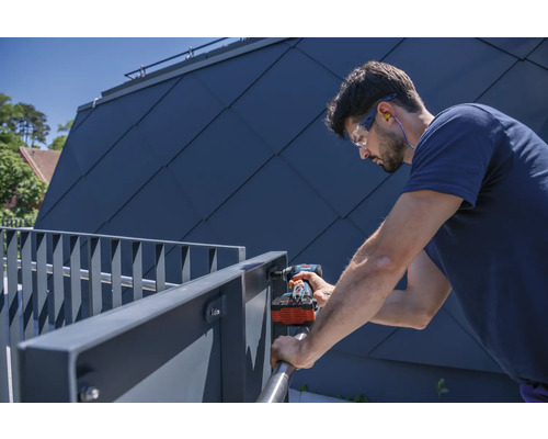 Ein Mann montiert ein Metallgeländer mit einem Akkuschrauber, wobei er Schutzbrille und Gehörschutz trägt.