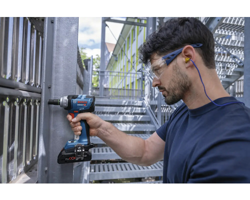 Handwerker mit Schutzbrille und Gehörschutz arbeitet mit einem Akku-Drehschlagschrauber an einer Metallkonstruktion.