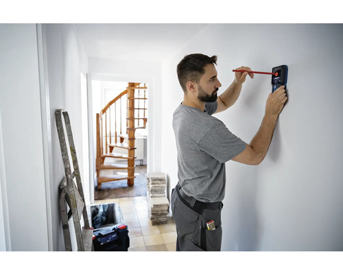 Mann benutzt einen Detektor zum Auffinden von Objekten in einer Wand in einem Haus.