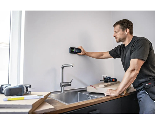 Mann verwendet einen digitalen Detektor an einer Wand in einer Küche.