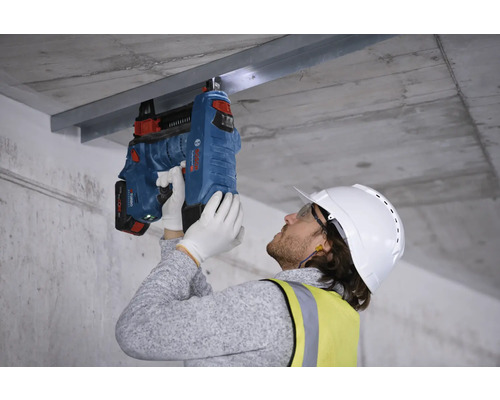 Ein Arbeiter befestigt eine Metallschiene mit einem Bolzenschussgerät an einer Betondecke.