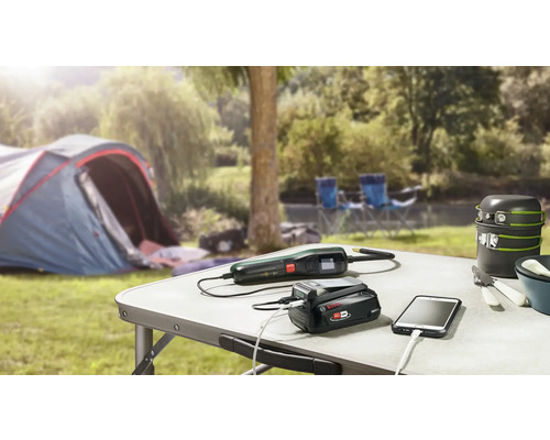 Campingszene mit Tisch, Zelt, Kochgeschirr, Ladegerät, Gartenschere und Smartphone
