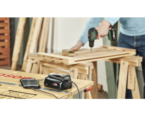 Szene einer Werkstatt mit Ladegerät, Handy und einer Person, die mit einem Akkuschrauber arbeitet