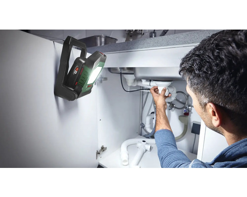 Mann repariert Abfluss unter Spüle mit Bosch Lampe