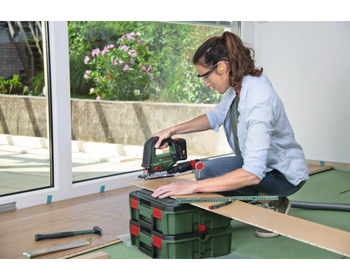 Frau schneidet Laminat mit einer Stichsäge, mit Sicherheitsbrille und Gehörschutz, Laminatverlegung auf dem Boden