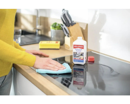 Eine Person reinigt ein Glaskeramikkochfeld mit einem Reinigungsmittel und einem Tuch.