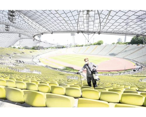 Eine Person desinfiziert Sitze in einem Stadion mit einem Desinfektionsmittel-Sprühgerät.