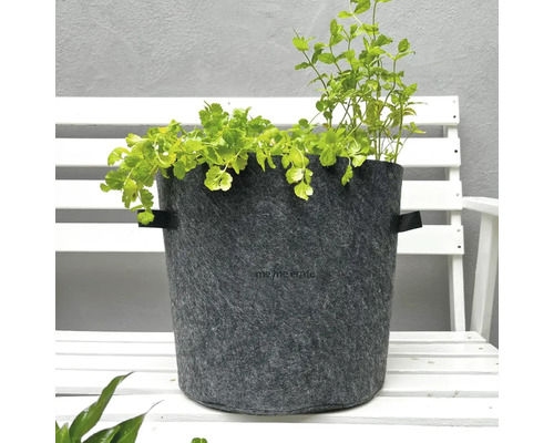 Grauer Pflanztopf aus Filz mit zwei Griffen und grünen Pflanzen auf einer weißen Bank
