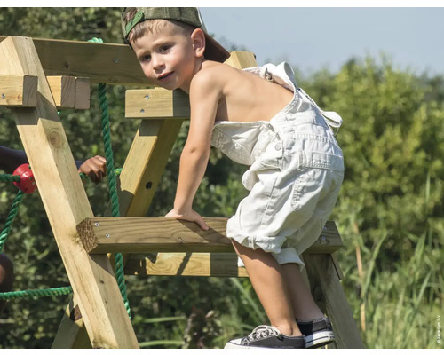 Junge klettert auf ein Holzspielgerät im Garten.