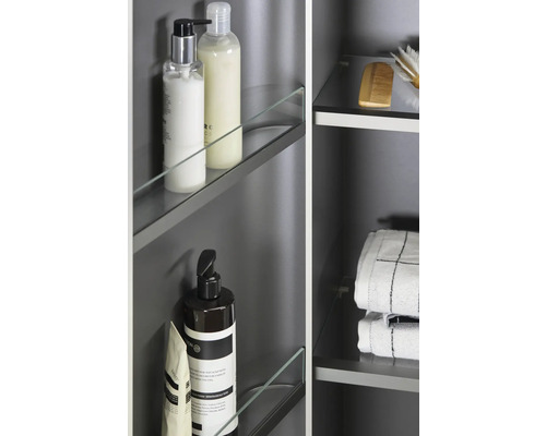 Detailansicht eines Badezimmerschranks mit Glasablagen und verschiedenen Badartikeln wie Handtüchern, Bürsten und Pflegeprodukten.