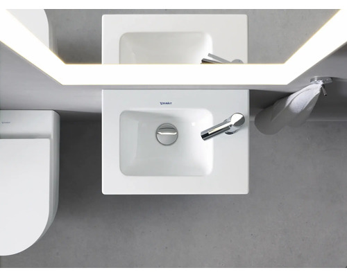 Ansicht von oben eines Badezimmers mit Waschbecken, Spiegel mit Beleuchtung, Handtuch und Toilette.