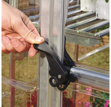Hand betätigt einen schwarzen Verschlussriegel an einem Gewächshausfenster.