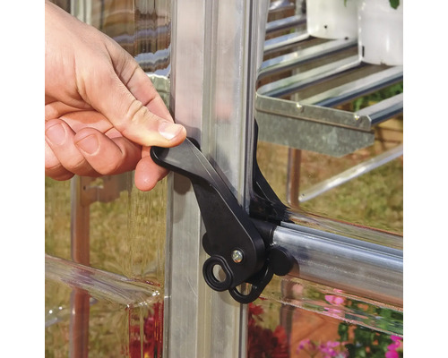 Hand betätigt einen schwarzen Verschlussriegel an einem Gewächshausfenster.